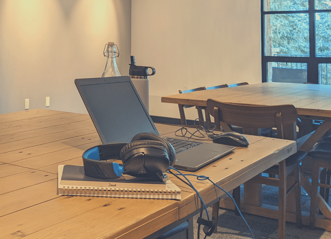 a laptop, headphones, mouse, and notebooks sitting on a wooden table